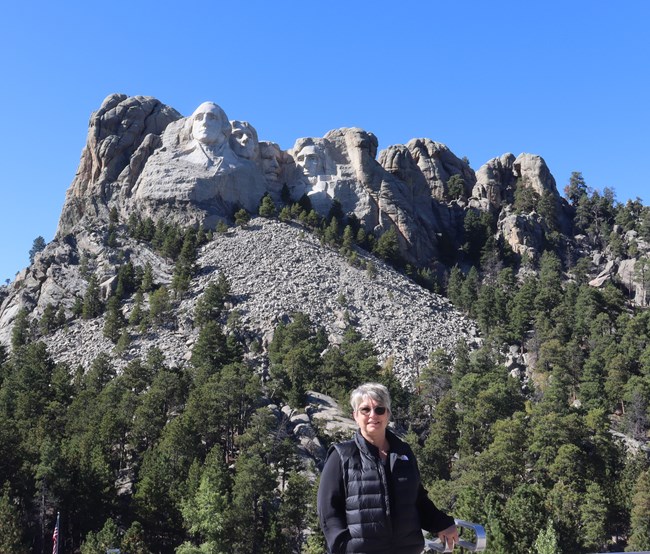 Smiling woman in black vest stands in front of Mount Rushmore