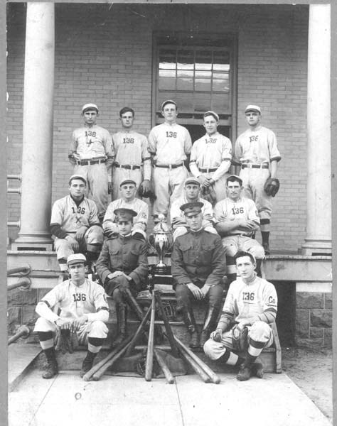 Young men in baseball uniforms sit with a trophy