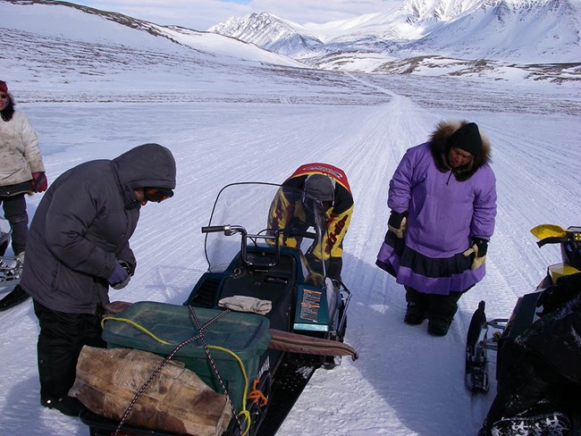 A group of people stop to check their snowmachines.