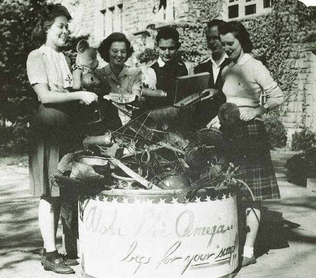 lt= four college students - women and one man - gathered around a bin holding scrap for a scrap drive