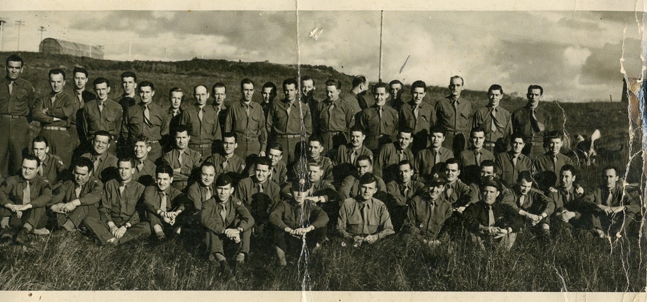 large group of men in uniform posing for a formal photo outside.