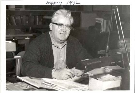 an older man sits at a desk with a pencil and papers