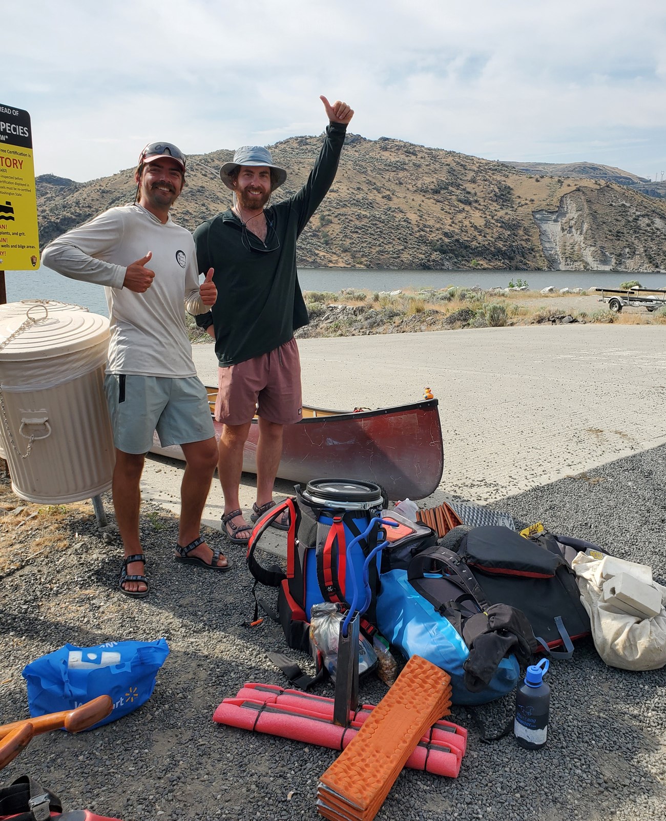 Joshua (left) and Anton (right) Two men stand next to a red canoe with all of their camping gear in front of them.