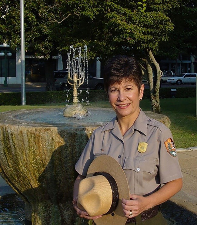 Superintendent Josie Fernandez Josie Fernandez poses with her NPS uniform with flat hat in her hand, standing in front of a hot spring.