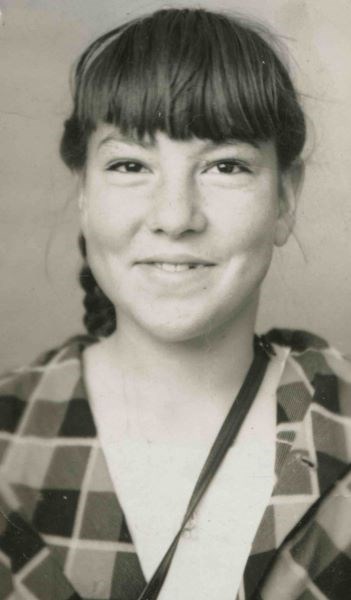 black and white photo of a young woman with bangs, smiling at the camera and wearing a plaid shirt