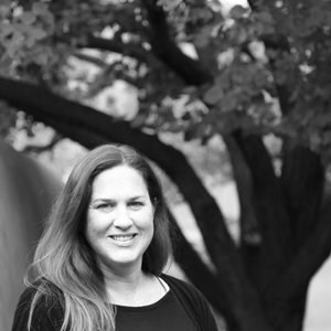 A black and white photo of the speaker standing beside a tree.