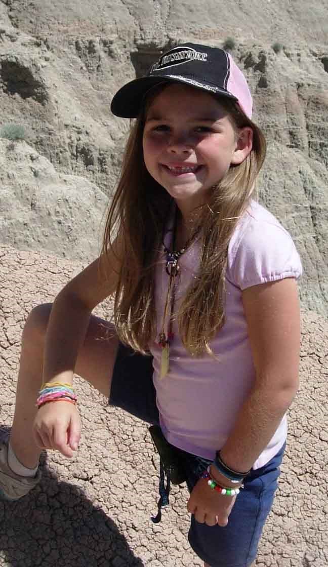 a young girl in a pink shirt and ballcap stands on badlands formations