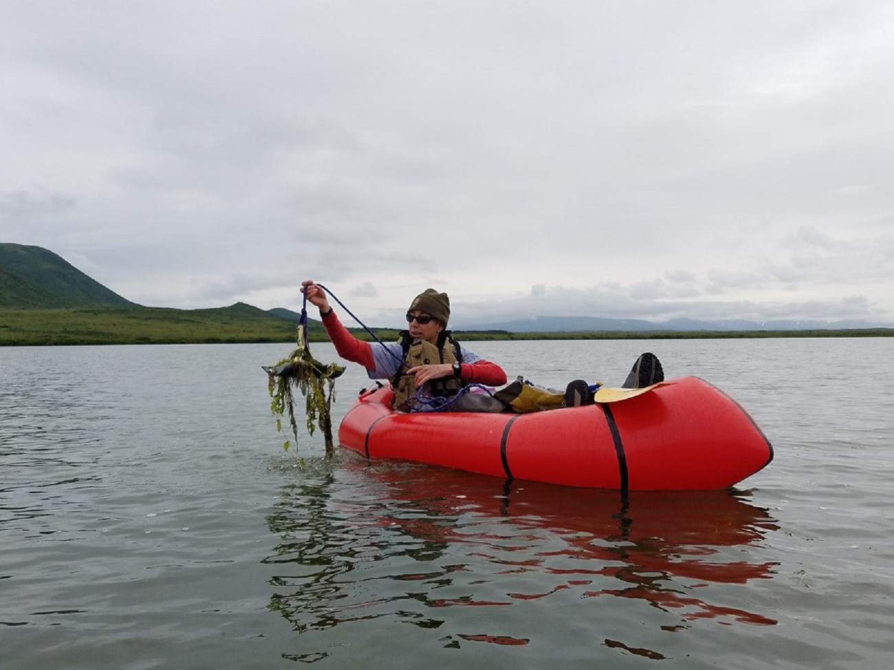 a person in an inflatable boat holds up an anchor covered in aquatic plants