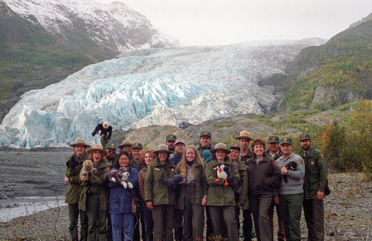 Several rangers in NPS uniform pose with puppets and Exit Glacier in the distance