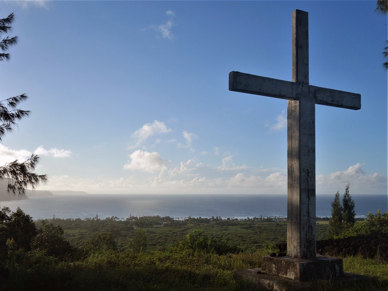Kauhakō Crater sunrise services Monument of cross stands overlooking lush landscape below and sunrise over Pacific ocean