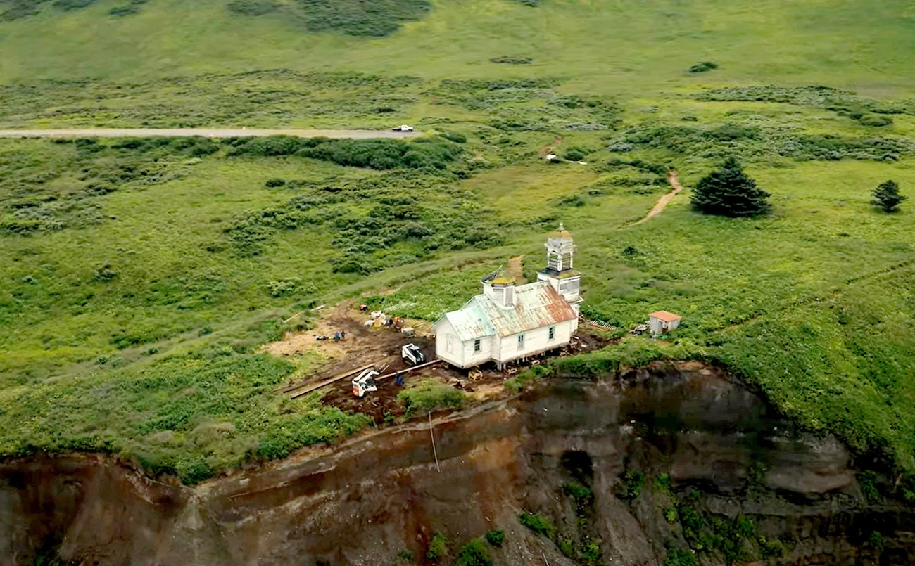 White church on the edge of a cliff with green pasture behind it