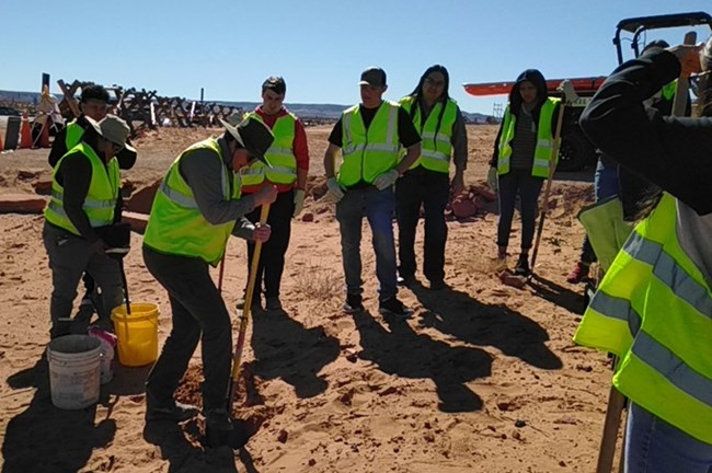 Park ranger and group of students in bright work vests dig holes on a trail