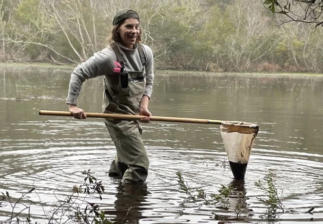 Katie Dagastino A woman in waders holding a net and standing in water