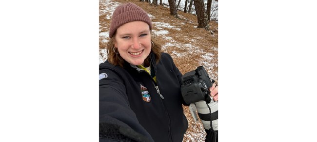 Katy Perrault Perrault in a selfie as she holds a large camera-lens combo on a lightly snowy trail.