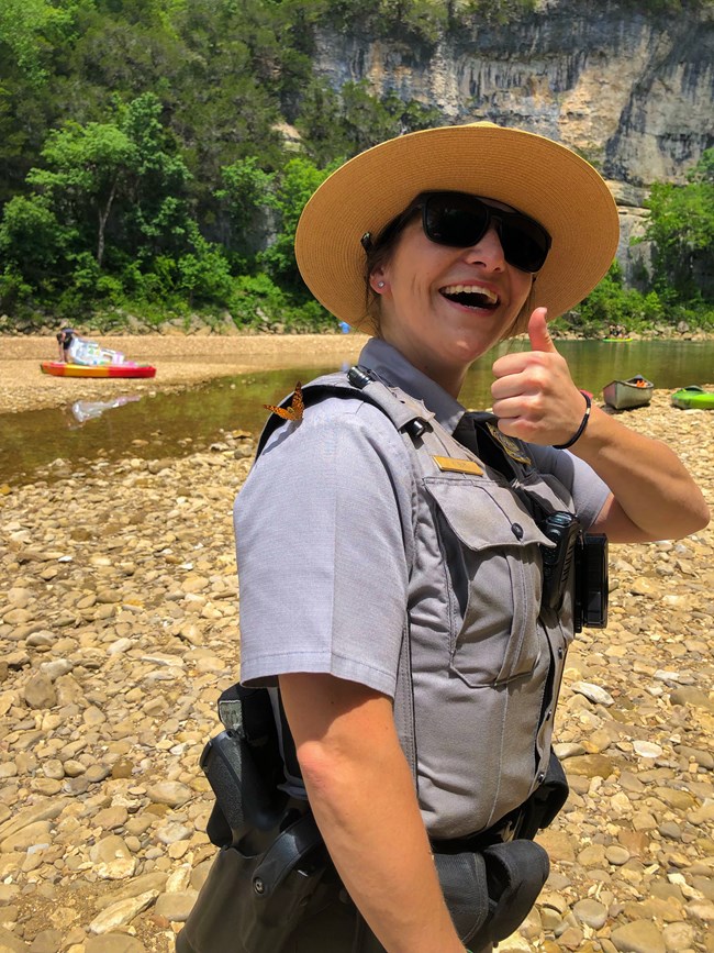 lt= A ranger in uniform smiling with a thumbs up and a butterfly on her shoulder.
