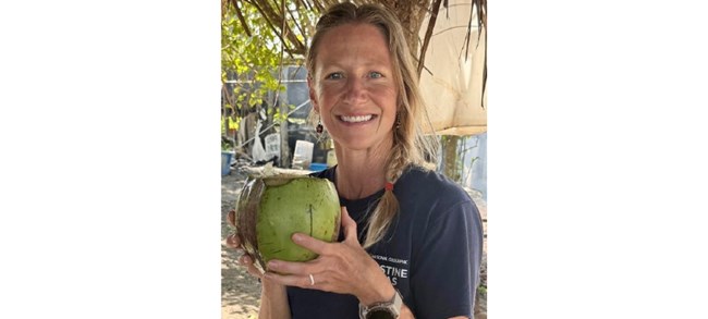 Kelly Moore Moore smiling at the camera, holding a coconut to drink from.