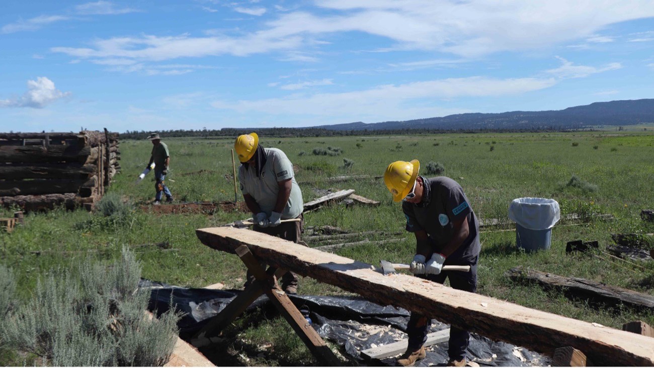 Kendrick Nahohai Two interns shape a long log with axes.