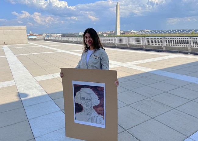 person holding a picture of a pencil drawing of a woman. Washington Monument is seen in the background