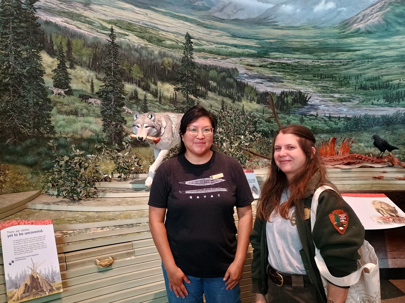 Kim Arthur and Crista Cummings Two people pose for a photo in front of a diorama featuring a wolf carrying a bloodied bone.
