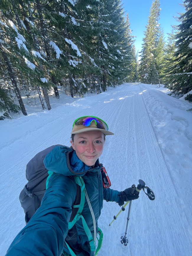 Smiling woman snowshoeing along snowy road in forest.