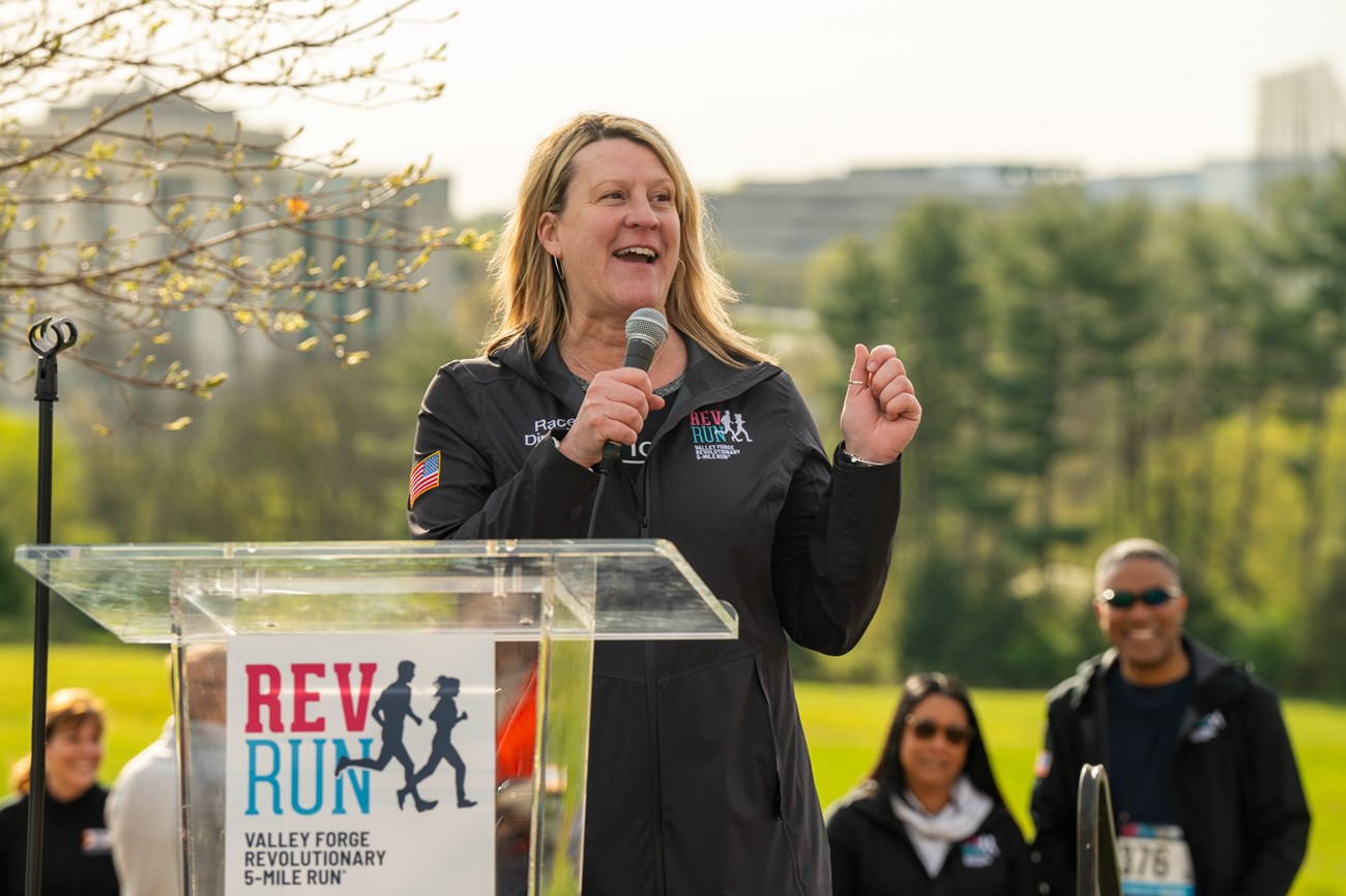 A person stands infront a podium that reads " Rev Run, Valley Forge Revolutionary 5 mile run"