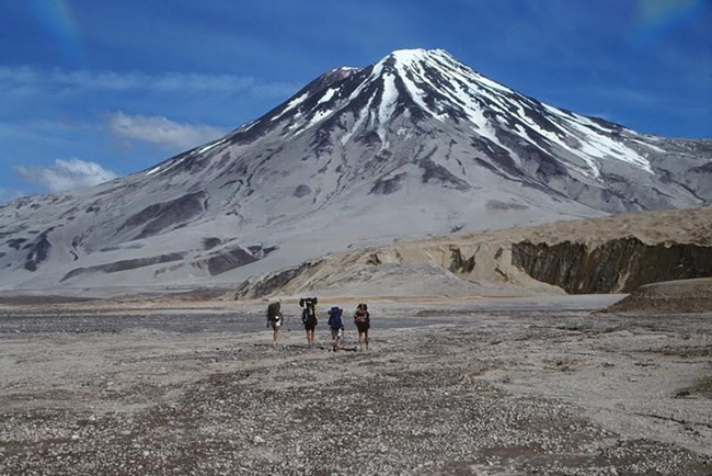 Knife Creek Glacier_alt photo from PK A group of four hikers walk toward a volcano.
