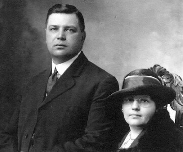Black and white photo of man in a suit and woman wearing dress clothes and hat with feather.