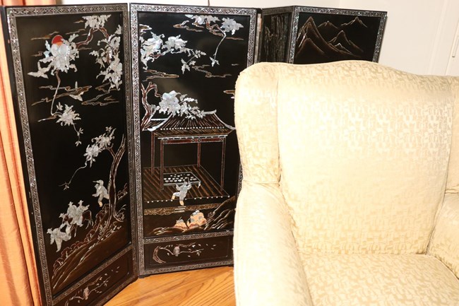 A color image showing a black folding screen with Korean inscriptions and artwork