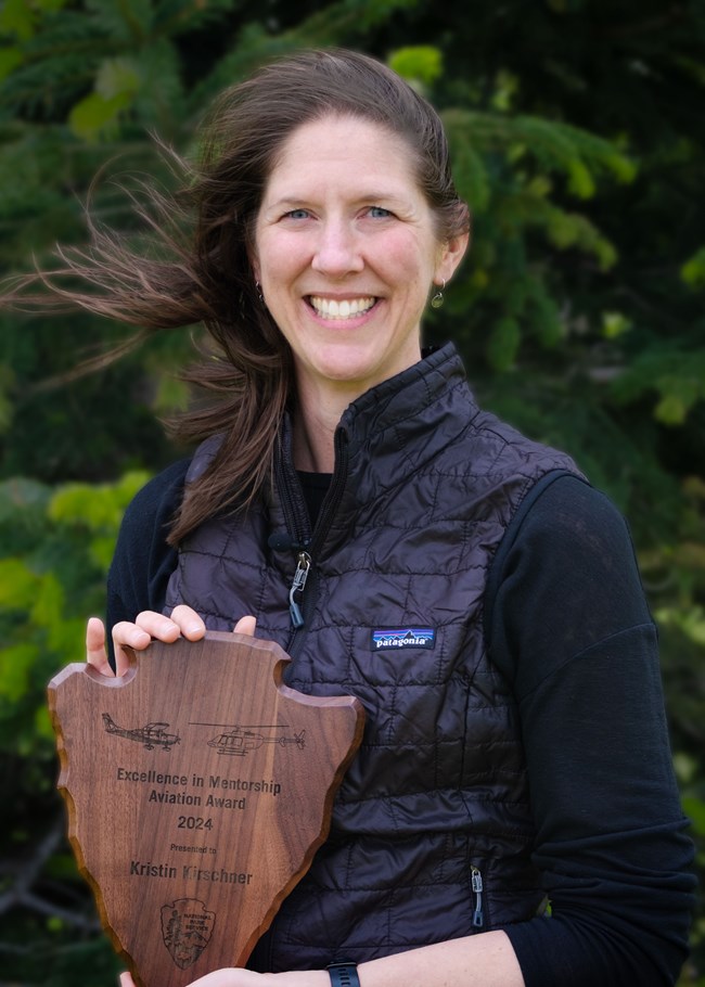 A women with brown hair holds an arrowhead plaque.