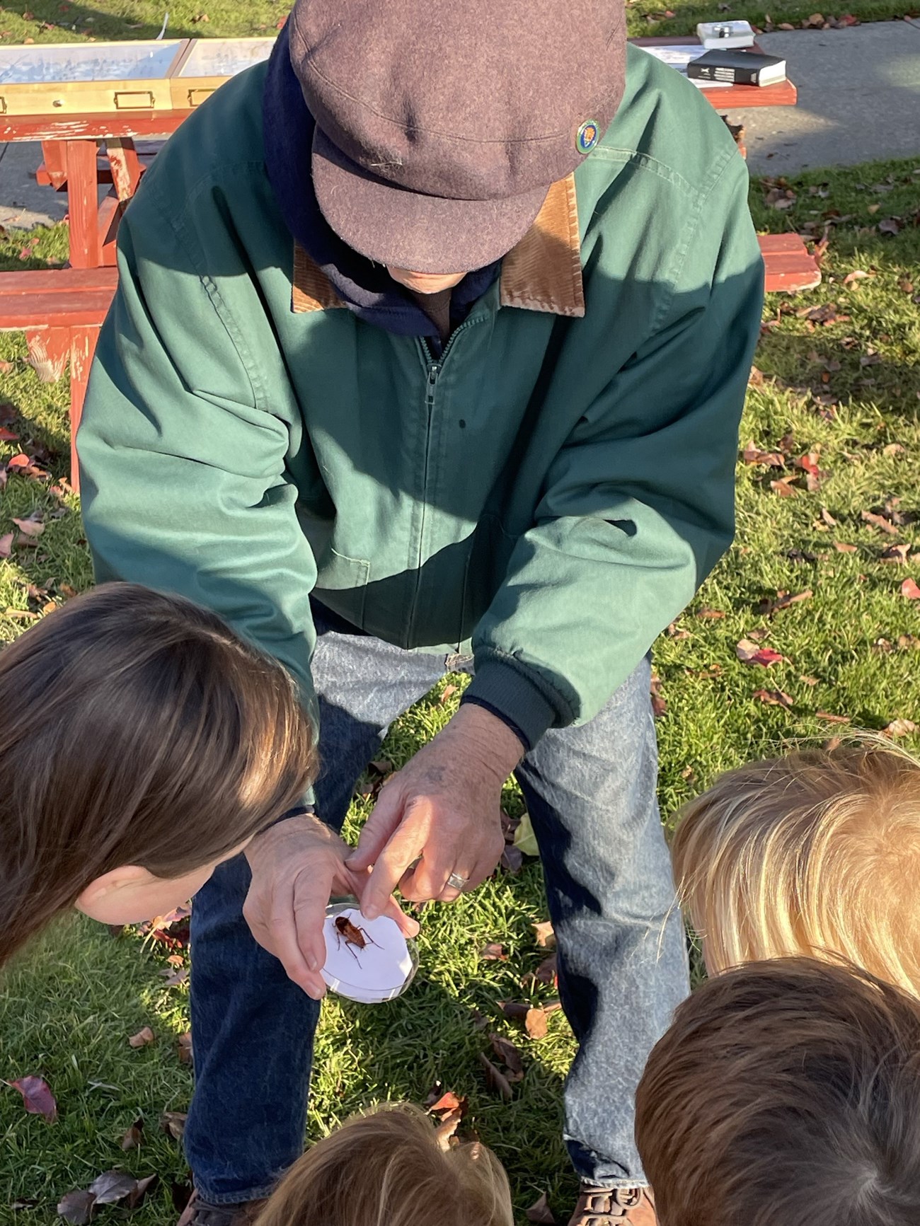 Cockroach on Display A man in a green jacket shows children a cockroach in a clear container.