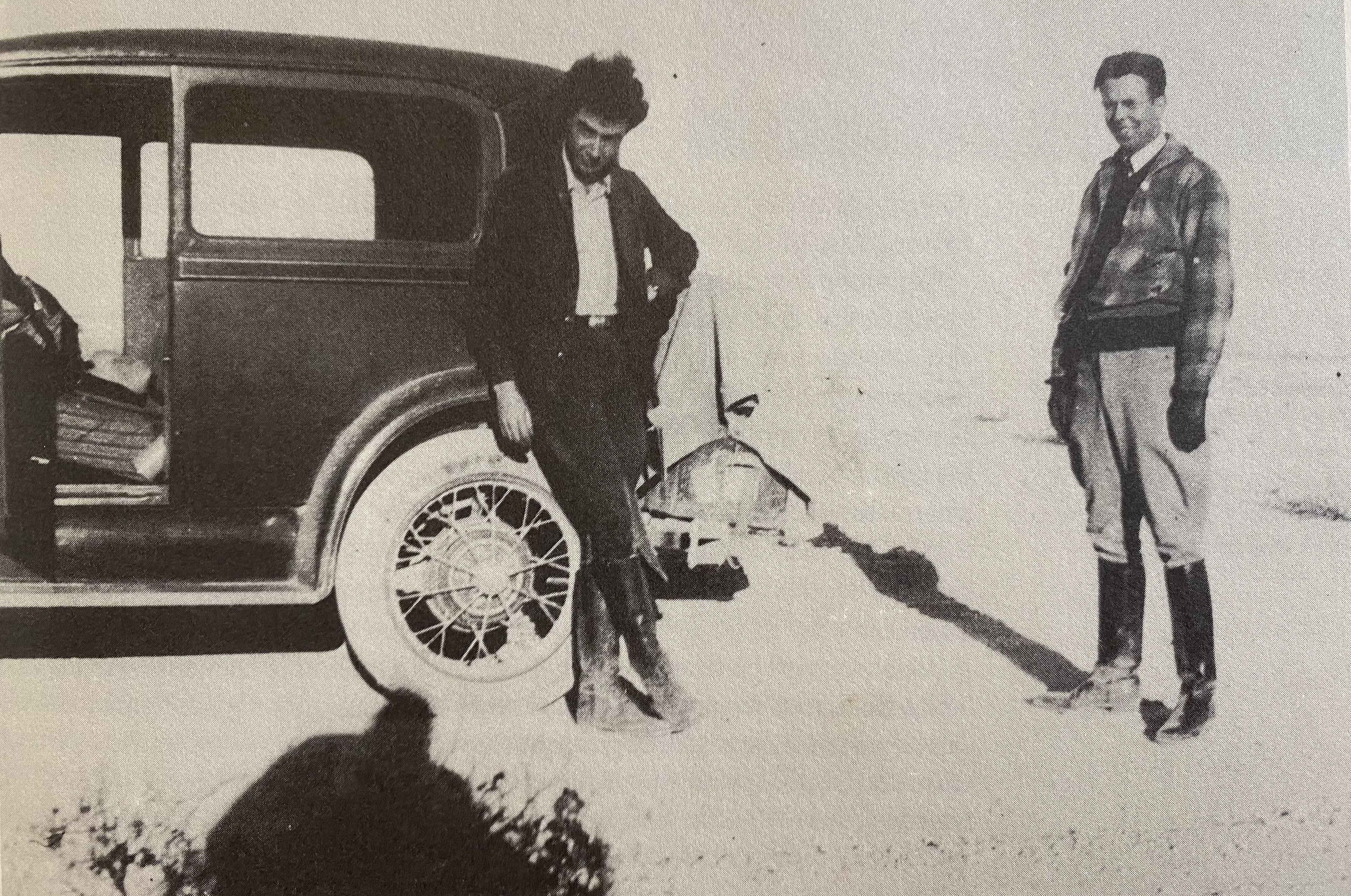 Black and white photo of Oppenheimer and Ernest Lawrence standing next to a car in the New Mexico desert.