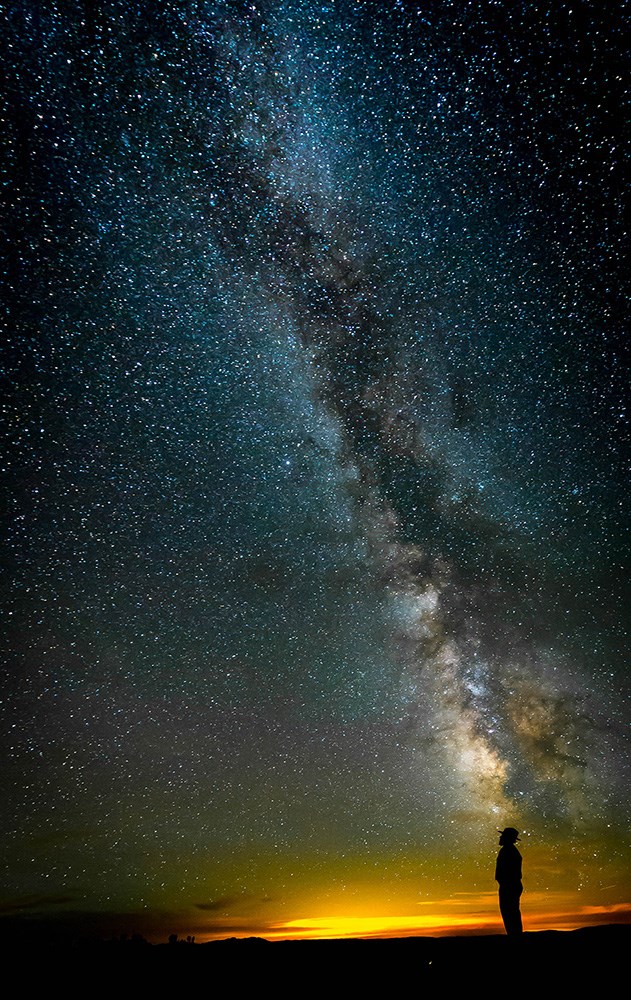 photo of a ranger in the foreground looking up at the milky way in the background