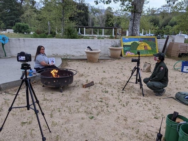 behind the scenes of Lei sitting down by a campfire reading a children's book while someone else films her with a camera
