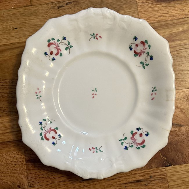 White ceramic plate with scalloped edges and red rose motif painted along rim