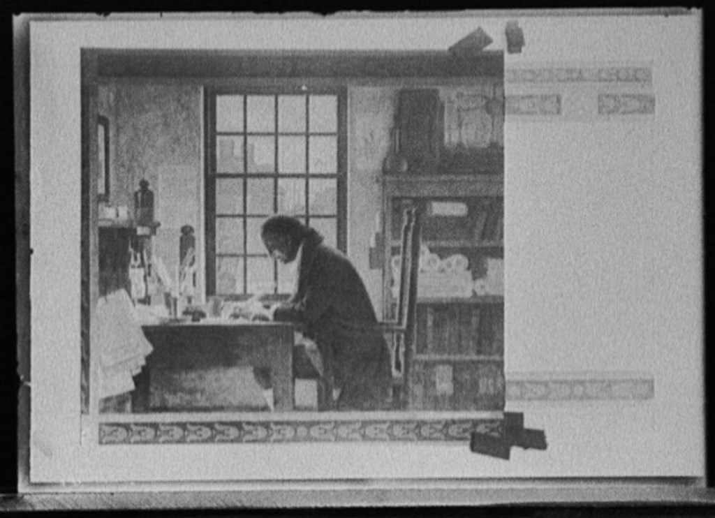 Benjamin Franklin seated at a writing desk working with a quill pen