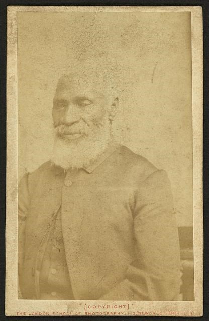 Faded photograph of an African American man with a white beard, wearing a dark colored frock coat.