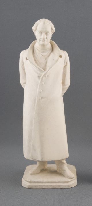 White plaster statuette of man standing wearing long coat