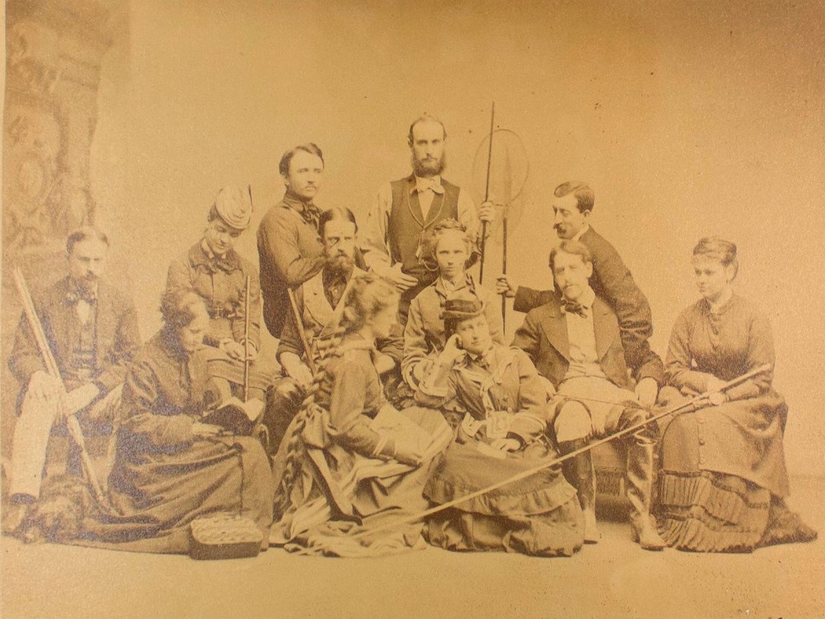 lt= Studio portrait of 12 men and women with fishing and hunting gear in formal clothing.