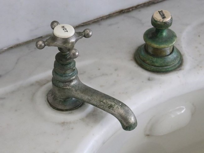 Detail view of faucet with four-pronged handle labeled hot on marble counter