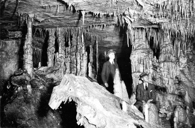 A black and white photo of two people looking at cave formations.