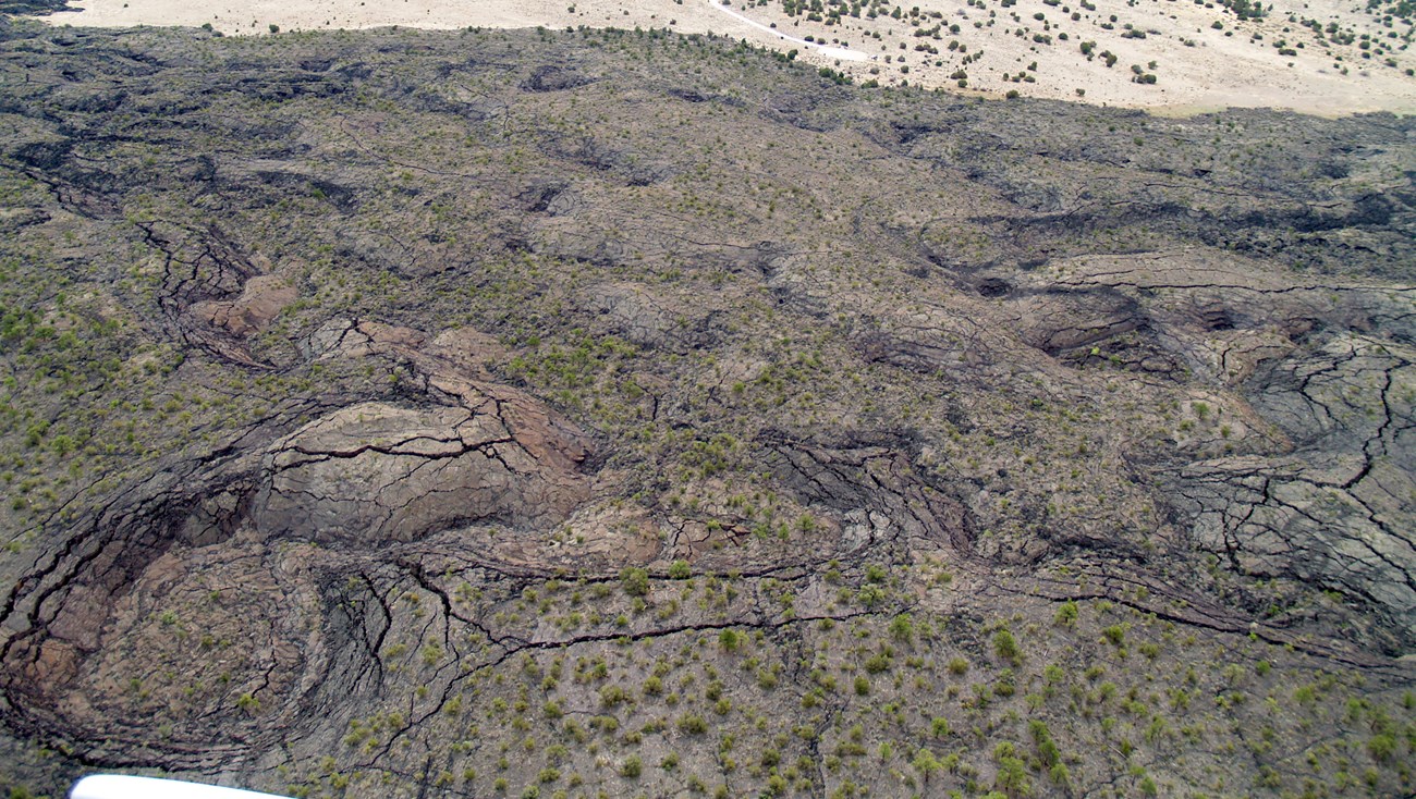 Aerial photo of a landscape covered with lava rock that has rounded pits and cracks.