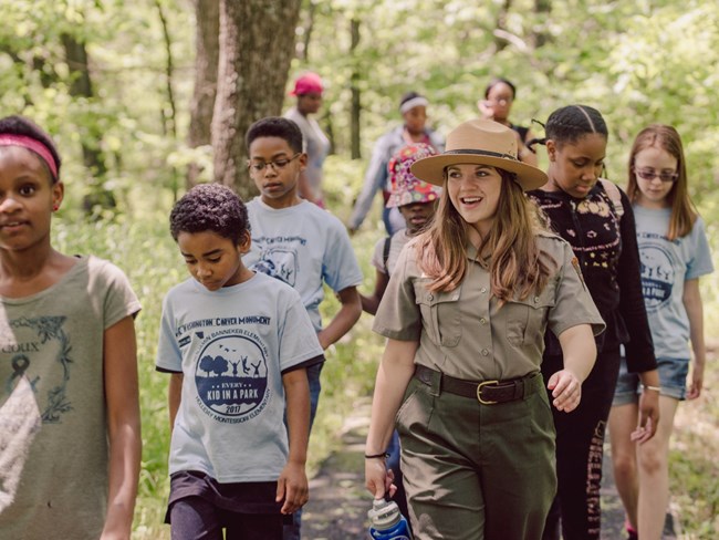 Ranger walking with six kids in a forest smiling