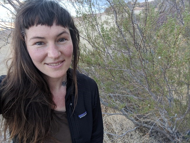 Lee Pipkin Woman smiling, standing next to desert shrubland vegetation.