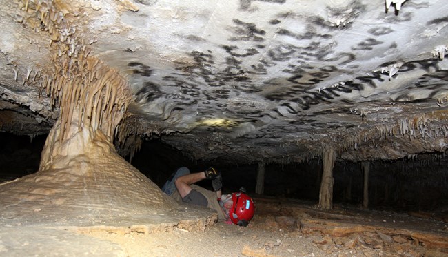 Researcher laying in a low section of the Lehman Caves taking pictures of historic signatures.
