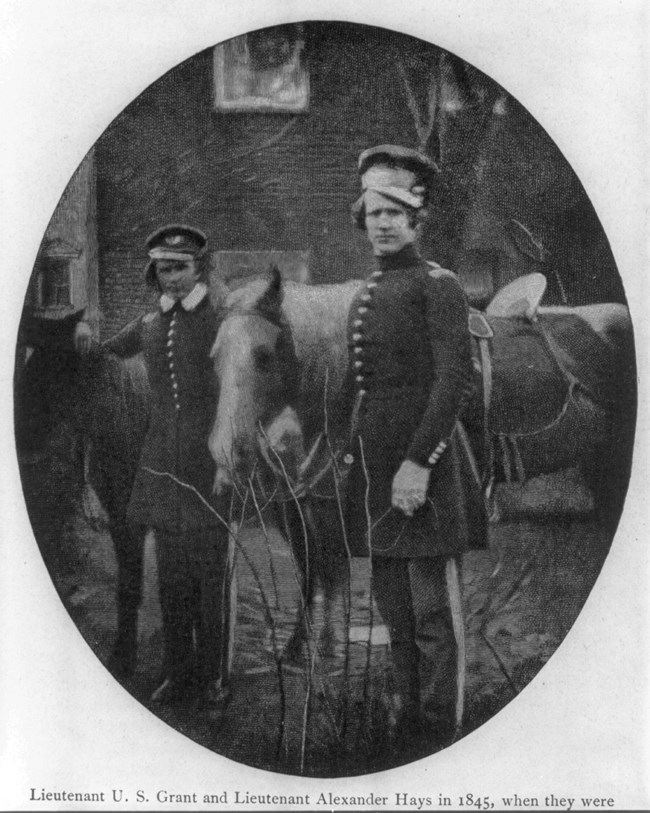 Black and white photo of two men behind and in front of a horse, while wearing military uniform