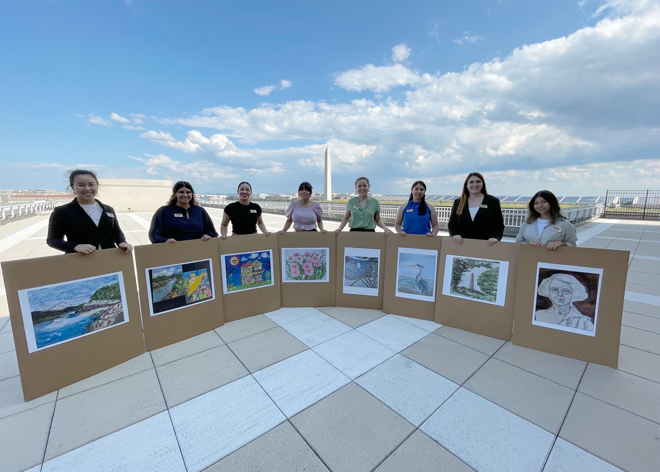 Interns with Artworks nine students holding pictures of their drawings and paintings with the washington monument in the background
