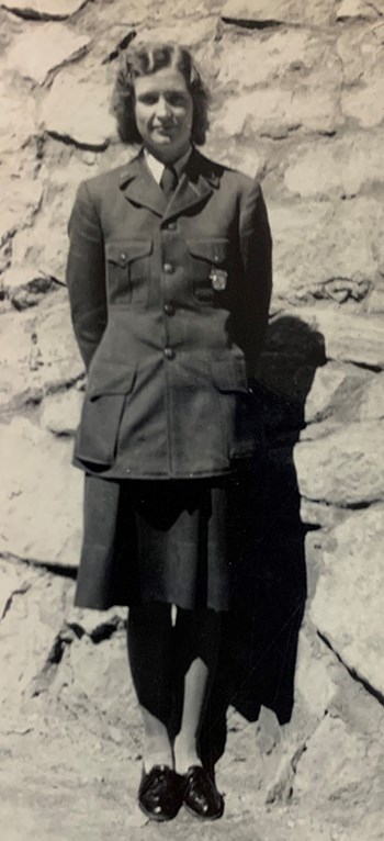 A woman wearing a skirt version of the NPS uniform stands in front of a stone wall.