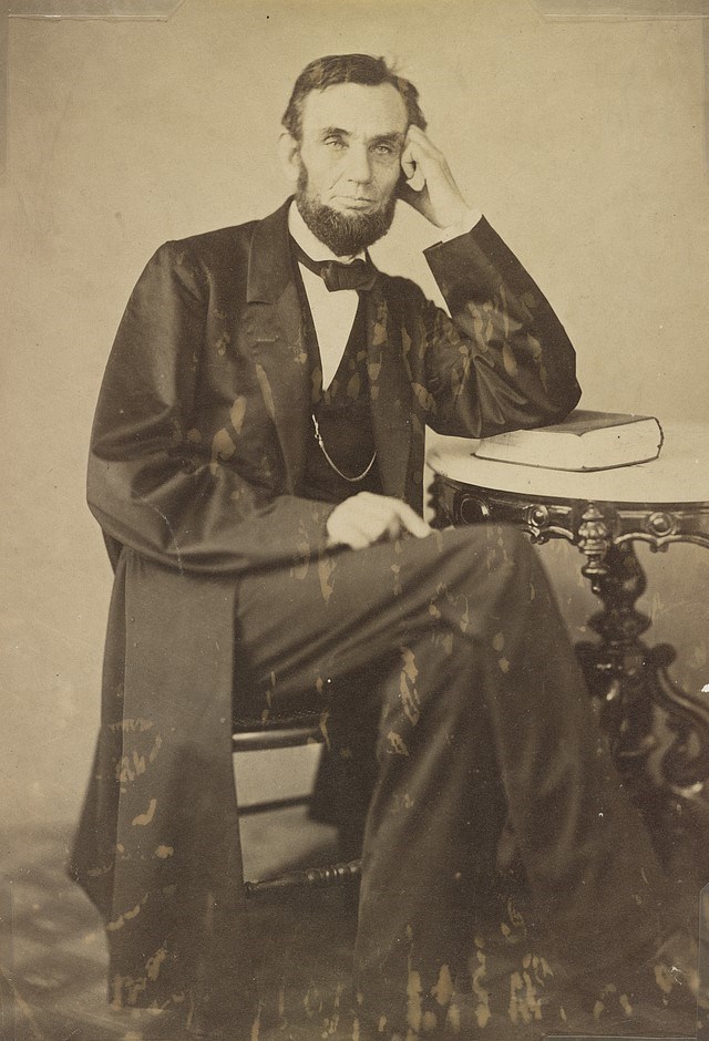 full-length portrait of Lincoln seated at a table and leaning on a book.
