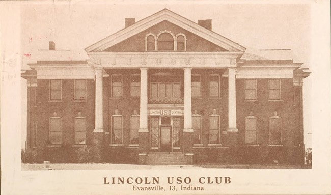 Sepia-toned photograph of a symmetrical brick building fronted with four white columns and a portico. A “Lincoln USO Center” banner is hung above the door between the columns.  The front of the building has two rows of windows.