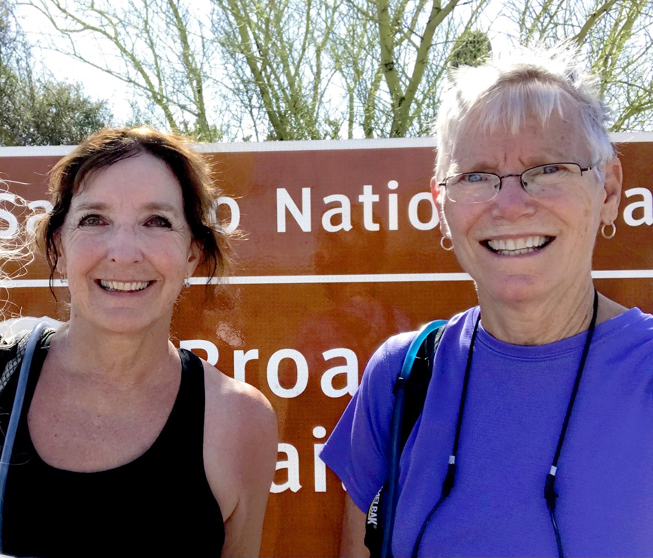 Two smiling women stand in front of a national park sign